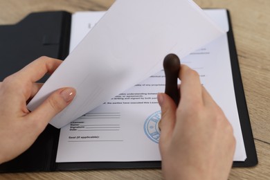 Photo of Woman stamping licensing agreement document at wooden table indoors, closeup