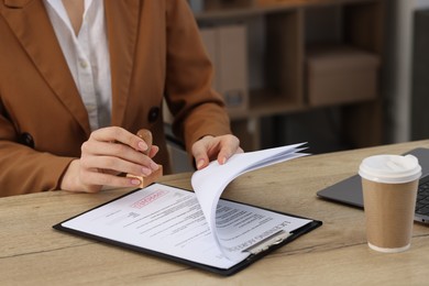 Photo of Woman stamping licensing agreement document at wooden table indoors, closeup