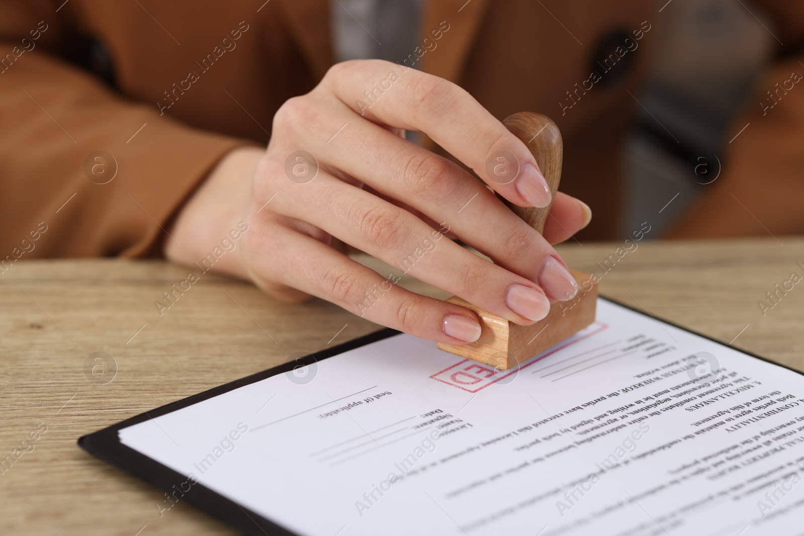 Photo of Woman stamping licensing agreement document at wooden table indoors, closeup