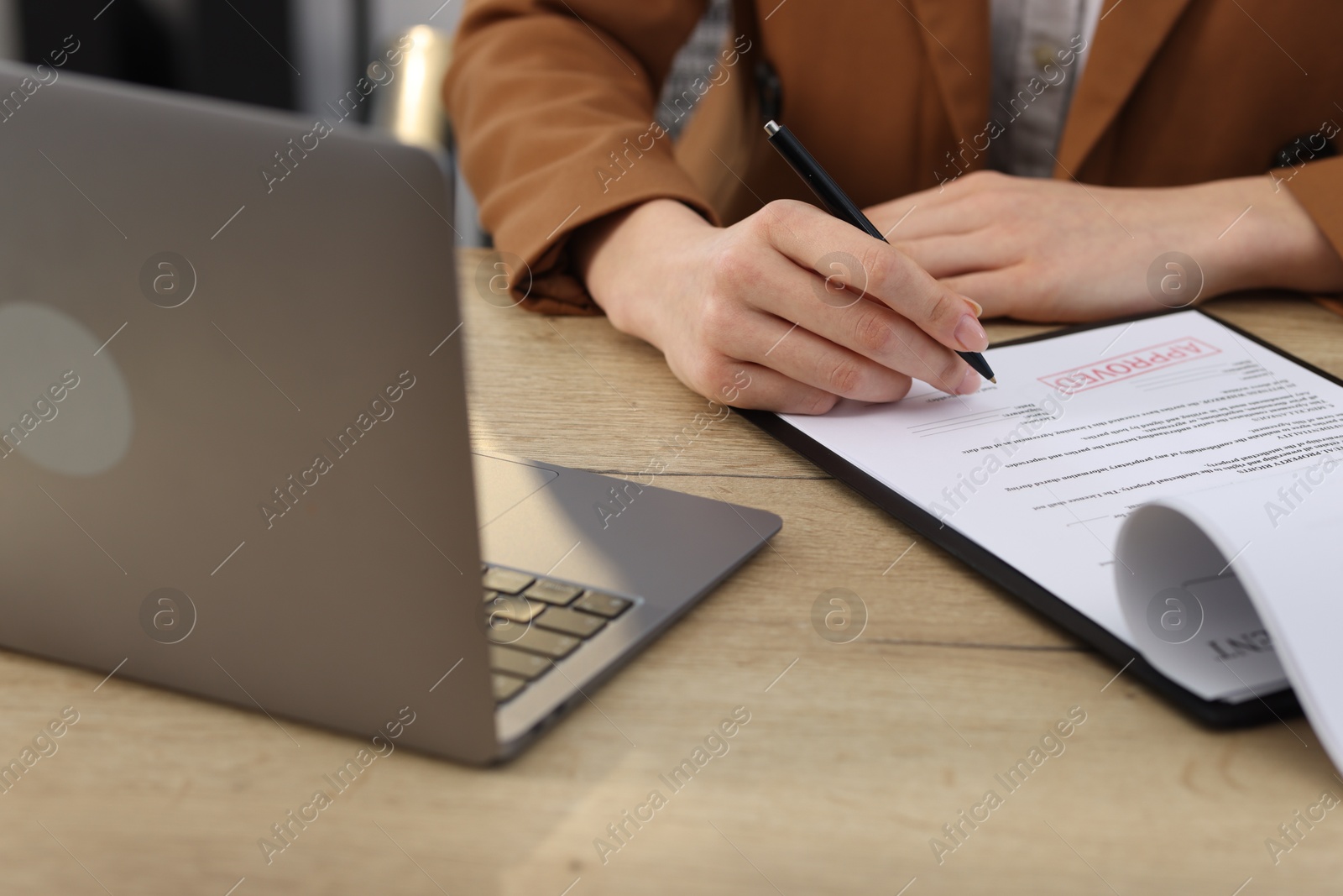 Photo of Woman signing licensing agreement document at wooden table indoors, closeup