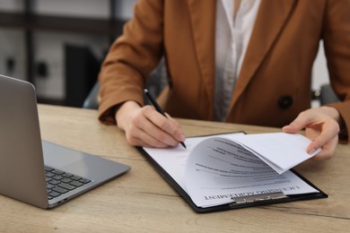 Photo of Woman signing licensing agreement document at wooden table indoors, closeup