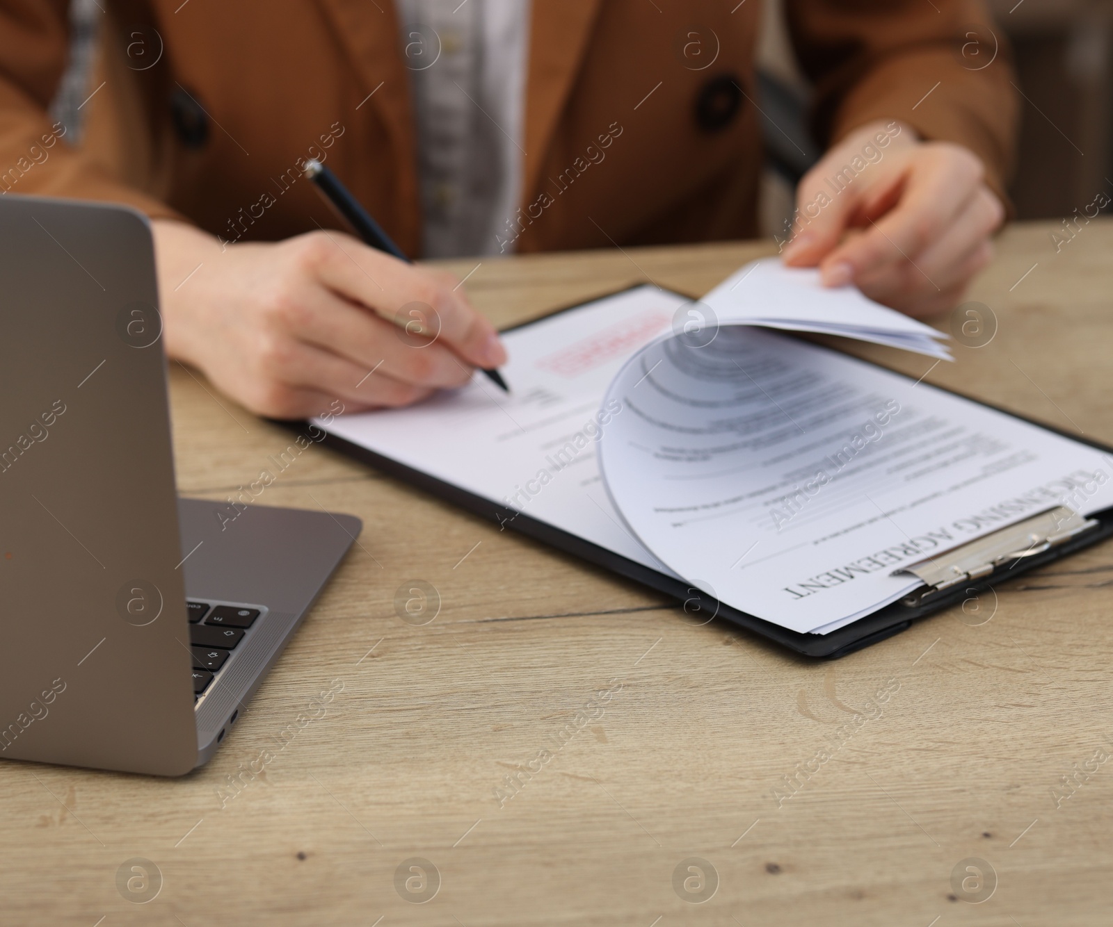 Photo of Woman signing licensing agreement document at wooden table indoors, closeup