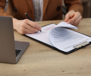 Photo of Woman signing licensing agreement document at wooden table indoors, closeup