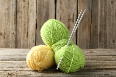 Photo of Skeins of colorful yarn and knitting needles on wooden table, closeup