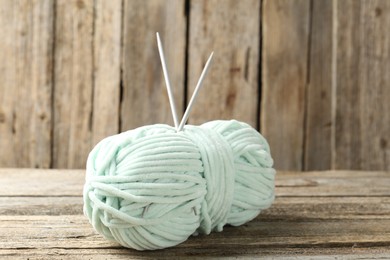 Photo of Skein of colorful yarn and knitting needles on wooden table, closeup