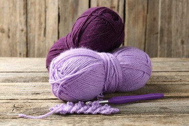 Photo of Skeins of colorful yarn, knitting sample and crochet hook on wooden table, closeup