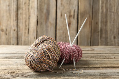 Photo of Skeins of colorful yarn and knitting needles on wooden table, closeup