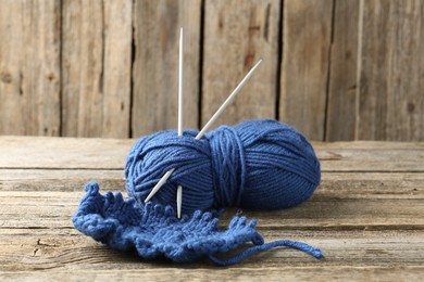 Photo of Skein of colorful yarn, sample and knitting needles on wooden table, closeup