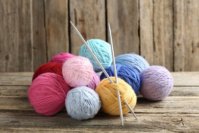 Photo of Balls of colorful yarn and knitting needles on wooden table, closeup