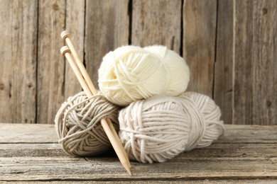 Photo of Skeins of yarn and knitting needles on wooden table, closeup