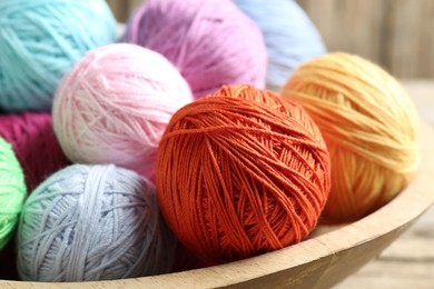 Photo of Balls of colorful yarn in bowl on wooden table, closeup