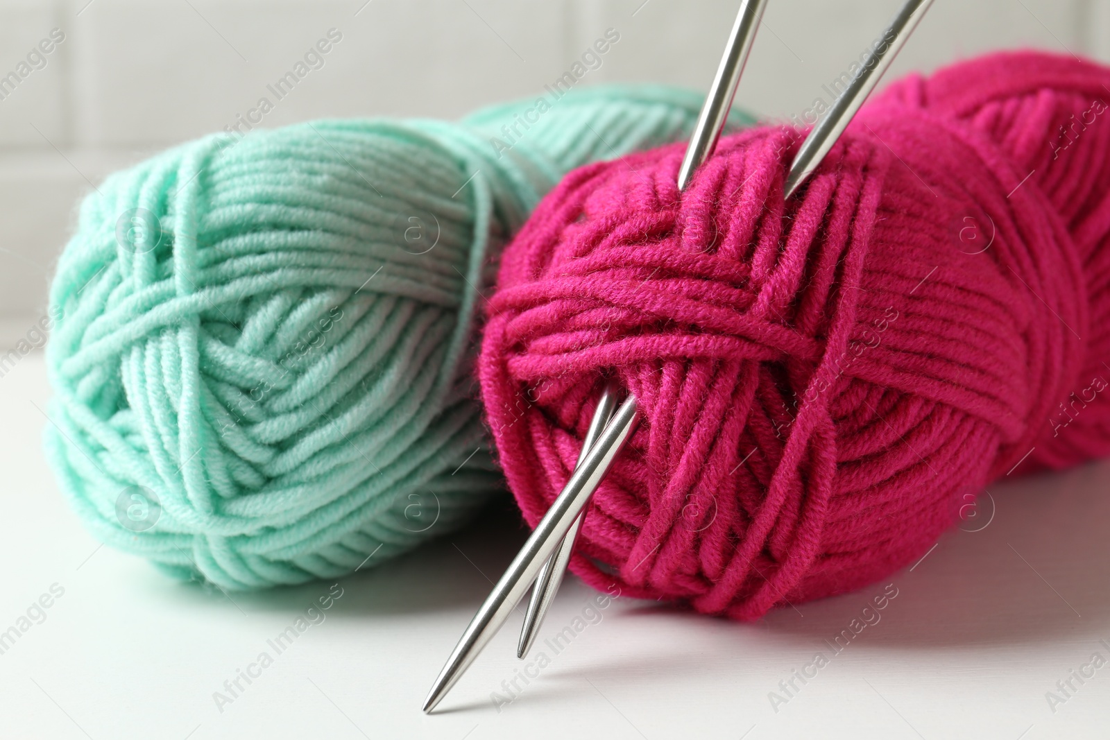 Photo of Skeins of colorful yarn and knitting needles on white table, closeup