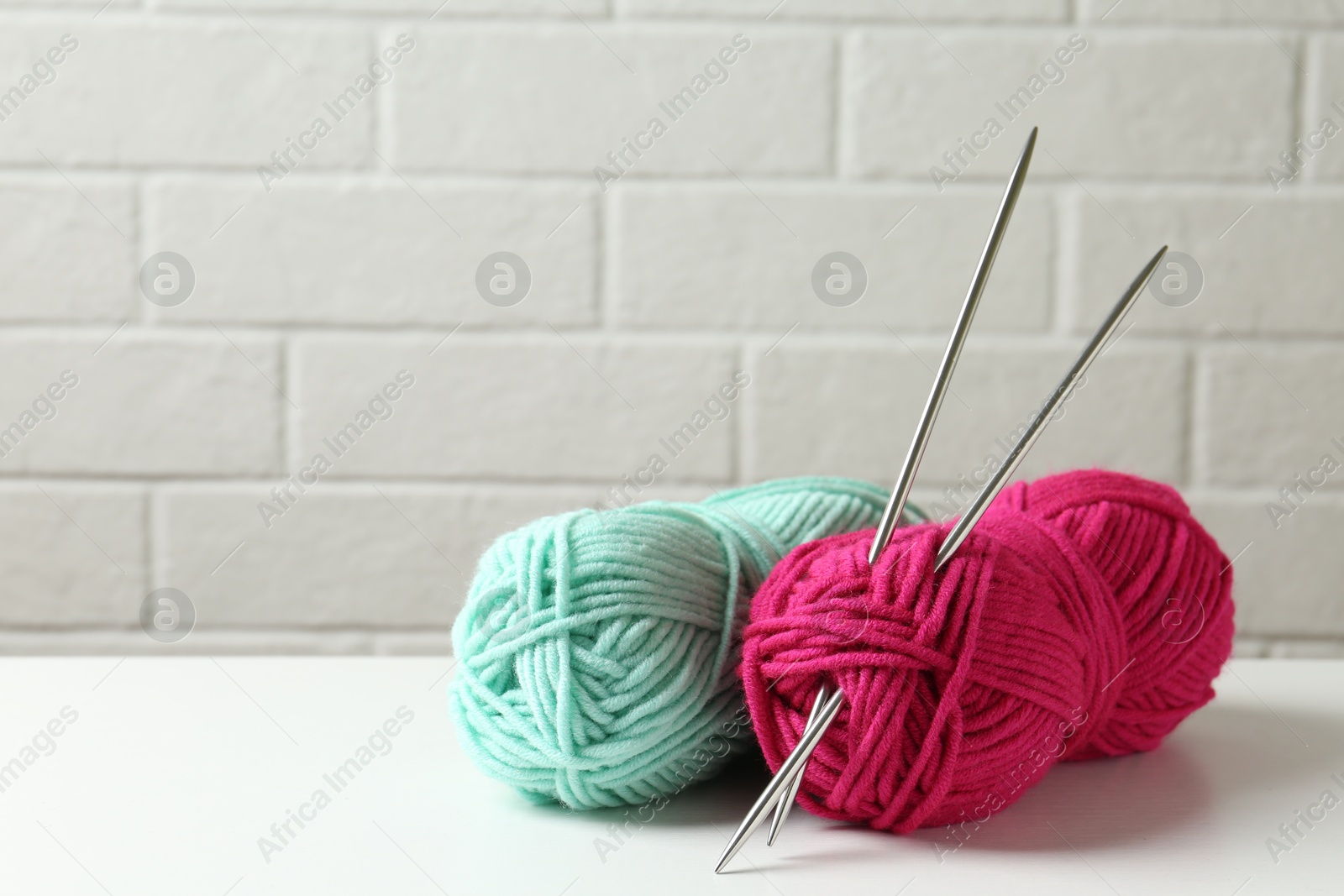 Photo of Skeins of colorful yarn and knitting needles on white table, closeup. Space for text