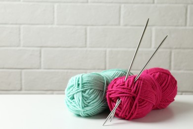 Skeins of colorful yarn and knitting needles on white table, closeup. Space for text