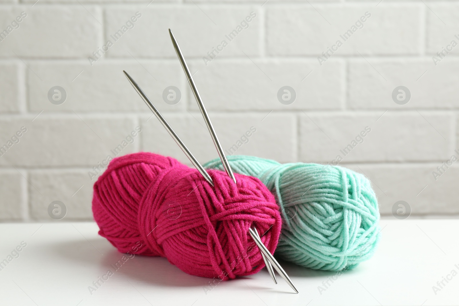 Photo of Skeins of colorful yarn and knitting needles on white table, closeup