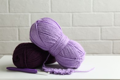 Photo of Skeins of colorful yarn, sample and crochet hook on white table, closeup. Space for text