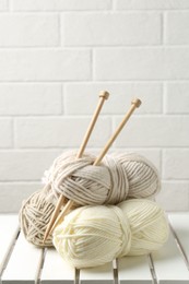 Photo of Skeins of yarn and knitting needles on white wooden table, space for text