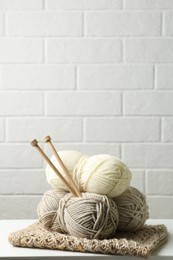 Photo of Skeins of yarn, knitted fabric and knitting needles on wooden table, space for text