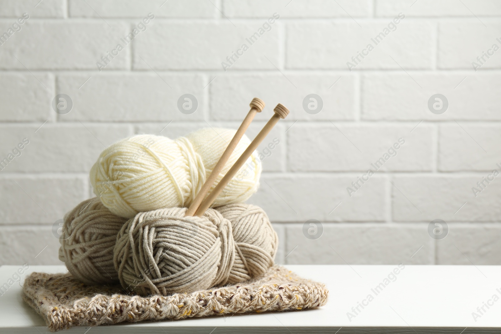 Photo of Skeins of yarn, knitted fabric and knitting needles on white wooden table, space for text