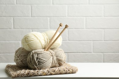 Photo of Skeins of yarn, knitted fabric and knitting needles on white wooden table, space for text