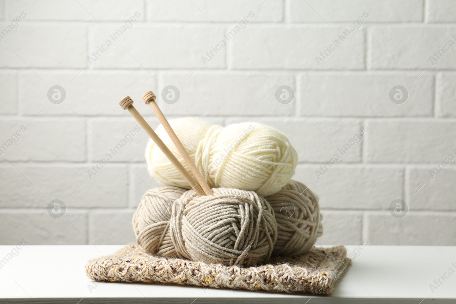 Skeins of yarn, knitted fabric and knitting needles on white wooden table Photo of Skeins of yarn, knitted fabric and knitting needles on white wooden table