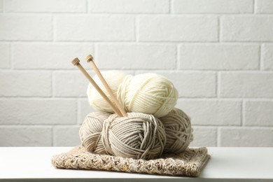 Photo of Skeins of yarn, knitted fabric and knitting needles on white wooden table