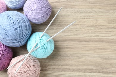 Photo of Balls of colorful yarn and knitting needles on wooden table, flat lay. Space for text