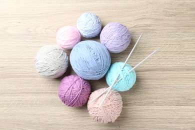 Photo of Balls of colorful yarn and knitting needles on wooden table, flat lay