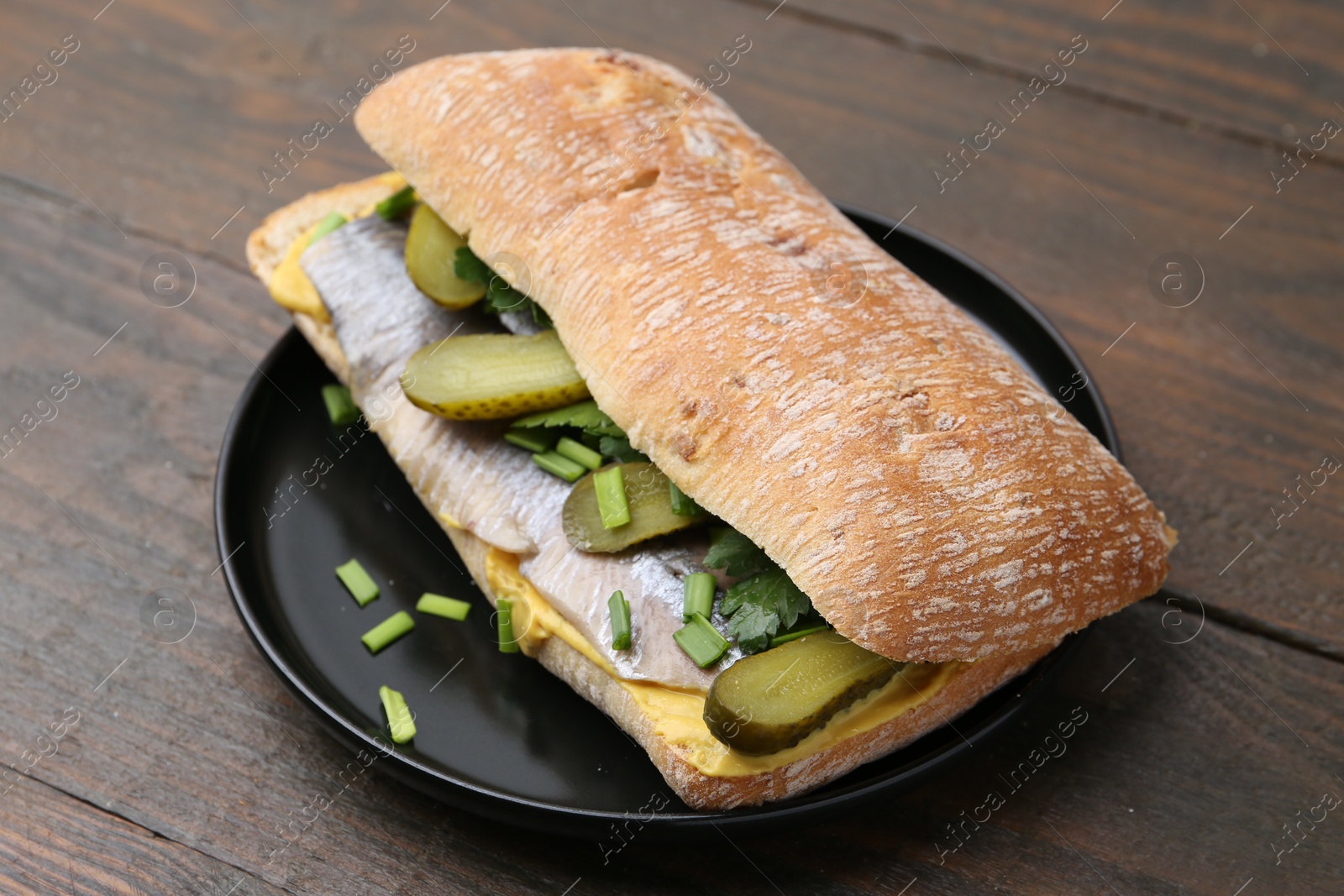 Photo of Tasty sandwich with herring, pickles, green onions and parsley on wooden table, closeup