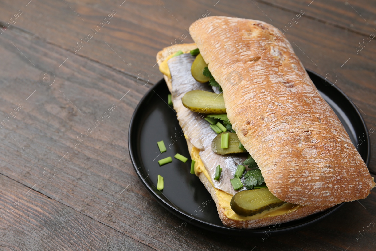 Photo of Tasty sandwich with herring, pickles, green onions and parsley on wooden table, closeup. Space for text