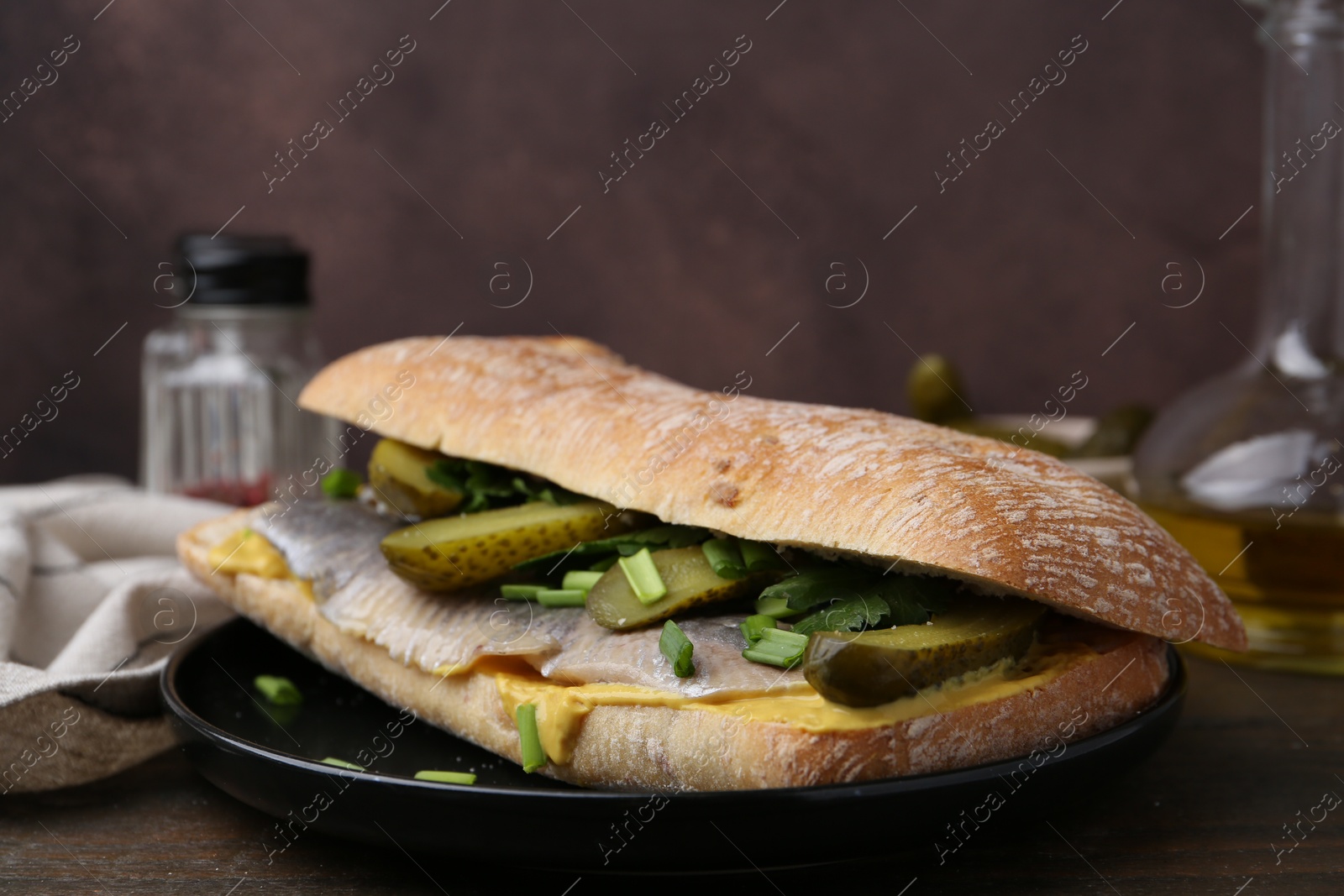 Photo of Tasty sandwich with herring, pickles, green onions and parsley on wooden table, closeup