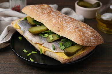 Photo of Tasty sandwich with herring, pickles, green onions and parsley on wooden table, closeup