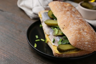 Tasty sandwich with herring, pickles, green onions and parsley on wooden table, closeup. Space for text