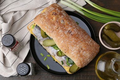 Tasty sandwich with herring, pickles, green onions and parsley on wooden table, flat lay