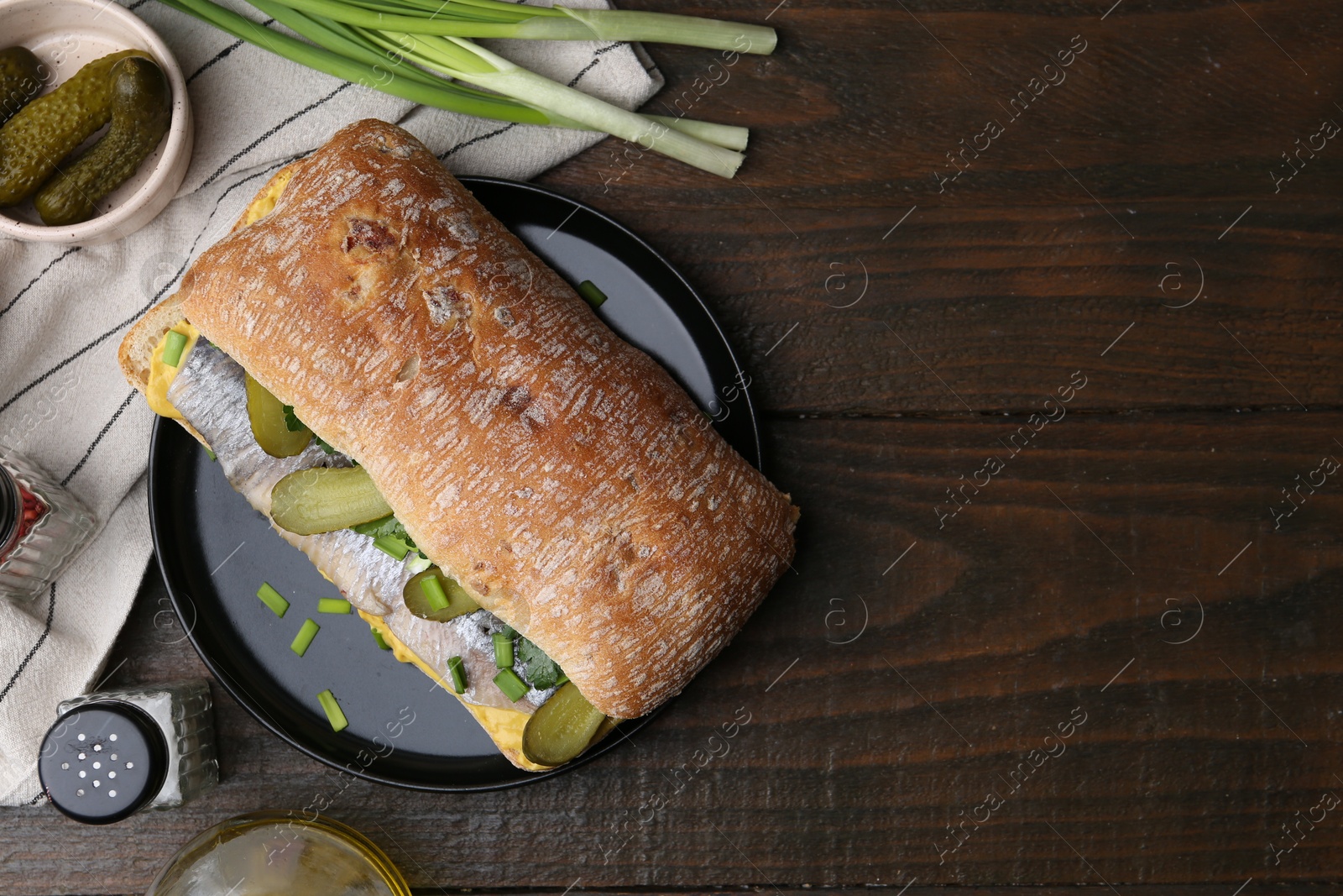 Photo of Tasty sandwich with herring, pickles, green onions and parsley on wooden table, flat lay. Space for text