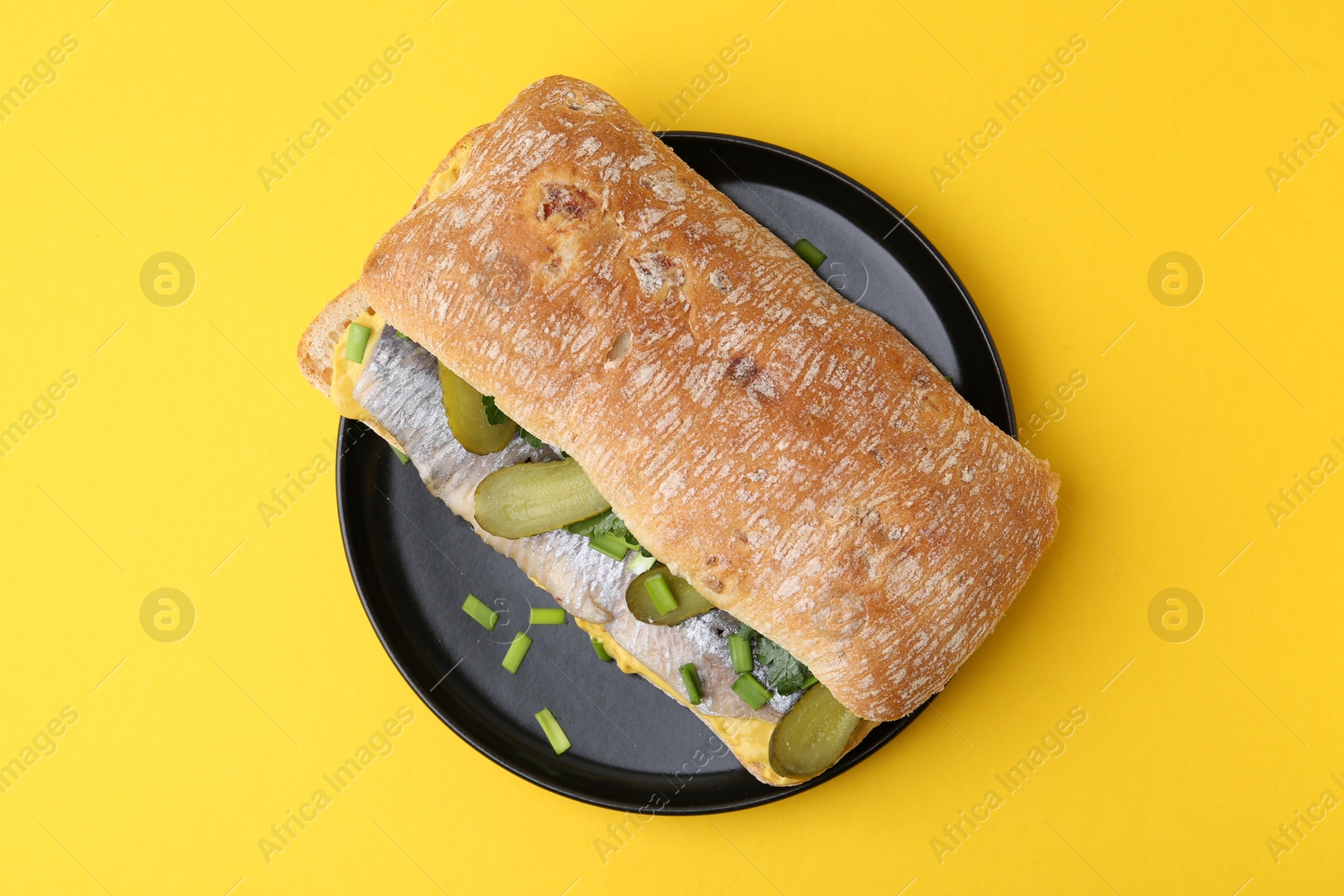 Photo of Tasty sandwich with herring, pickles, green onions and parsley on yellow background, top view