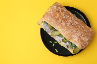 Tasty sandwich with herring, pickles, green onions and parsley on yellow background, top view. Space for text