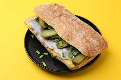 Tasty sandwich with herring, pickles, green onions and parsley on yellow background, closeup