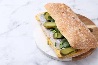 Photo of Tasty sandwich with herring, pickles, green onions and parsley on white marble table, closeup. Space for text