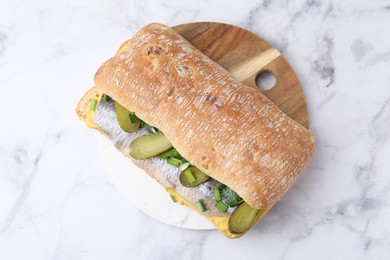 Photo of Tasty sandwich with herring, pickles, green onions and parsley on white marble table, top view