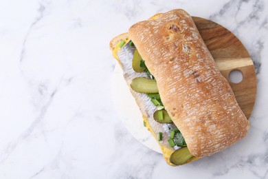 Tasty sandwich with herring, pickles, green onions and parsley on white marble table, top view. Space for text