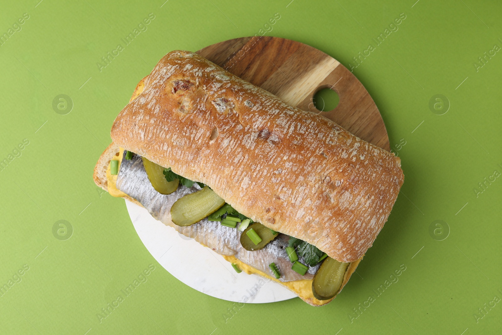 Photo of Tasty sandwich with herring, pickles, green onions and parsley on color background, top view