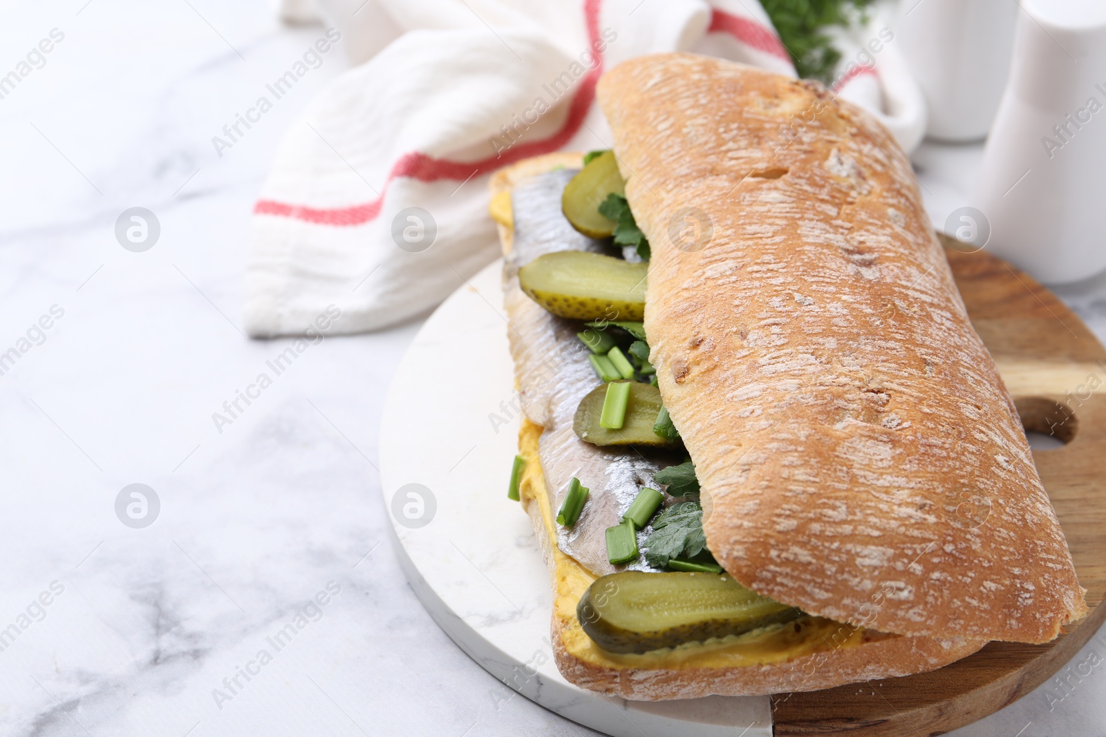 Photo of Tasty sandwich with herring, pickles, green onions and parsley on white marble table, closeup. Space for text