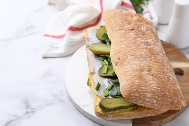 Tasty sandwich with herring, pickles, green onions and parsley on white marble table, closeup. Space for text