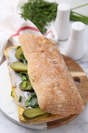 Tasty sandwich with herring, pickles, green onions and parsley on white marble table, closeup