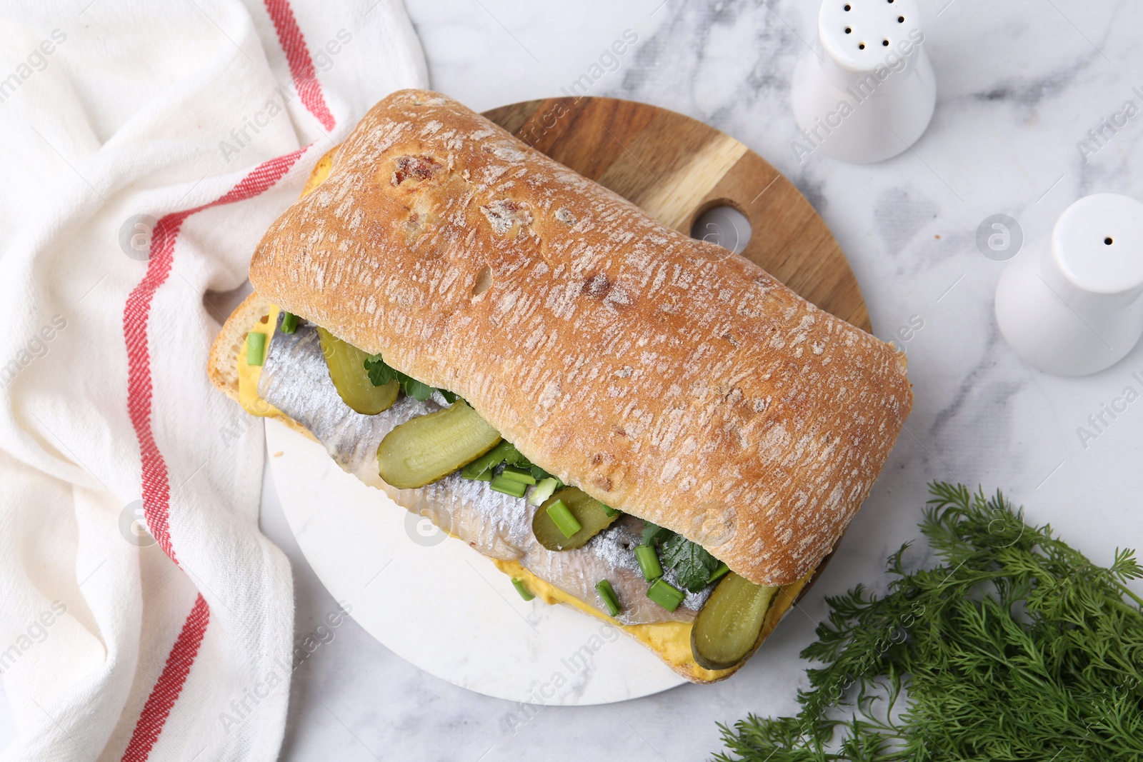 Photo of Tasty sandwich with herring, pickles, green onions, dill and parsley on white marble table, flat lay