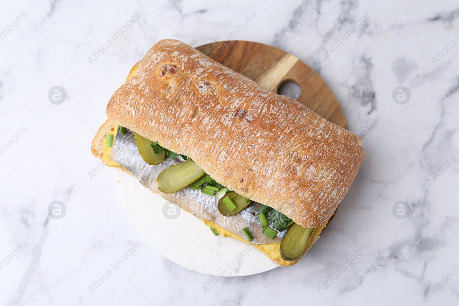 Photo of Tasty sandwich with herring, pickles, green onions and parsley on white marble table, top view