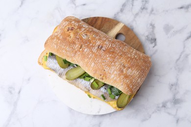 Tasty sandwich with herring, pickles, green onions and parsley on white marble table, top view