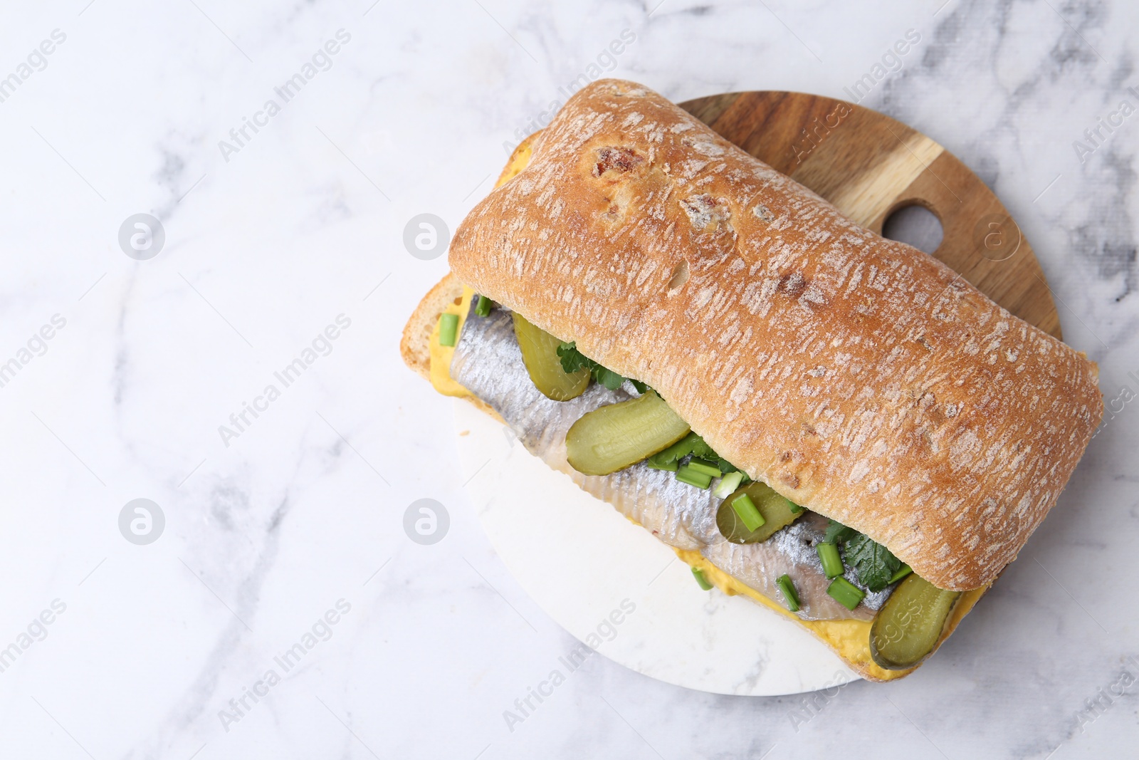 Photo of Tasty sandwich with herring, pickles, green onions and parsley on white marble table, top view. Space for text