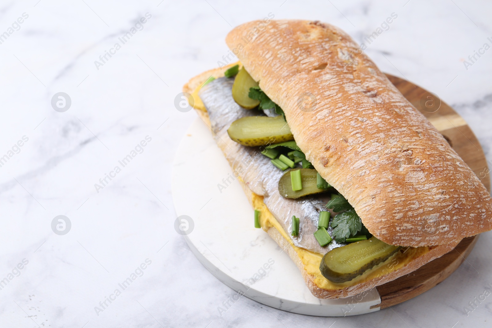 Photo of Tasty sandwich with herring, pickles, green onions and parsley on white marble table, closeup. Space for text